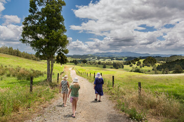 Three people are walking down a stony, dry path in beautiful countryside. This was taken in New Zealand. 