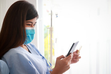 Asian female patient holding smartphone and credit card to pay medical bills. Finance concept,...