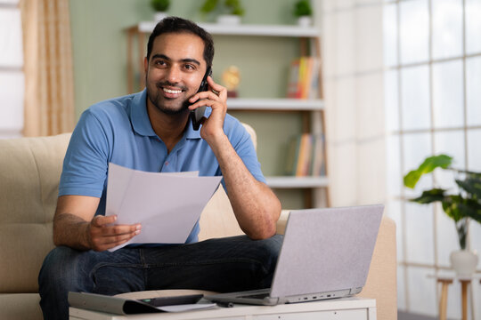 Happy Confident Indian Man Talking On Mobile Phone By Holding Insurance Or Property Documents At Home - Concept Of Business Deal, Job Interview And Promotion Joy