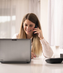 A girl at the office with the laptop talking on the phone and smiling