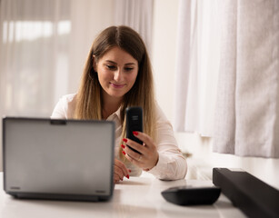 A girl at the office with the laptop looking at the phone and smiling