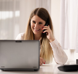 A girl at the office with the laptop talking on the phone and smiling