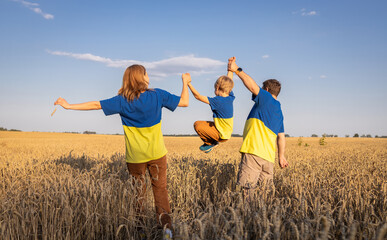 unrecognizable happy family in identical yellow - blue t-shirts stands among spikelets in wheat field in Ukraine, child bounces. national identity. Pride, support, faith in victory. Independence Day