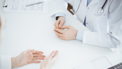 Doctor and patient discussing current health questions while sitting opposite of each other at the table in clinic, close up and above view. Medicine concept