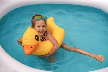 Funny laughing humorous girl having fun in the water in an inflatable mini swimming pool swimming...