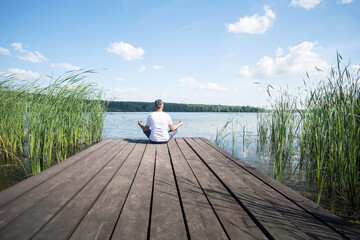 Back view of a man meditating on wooden pier near lake. Space for text.