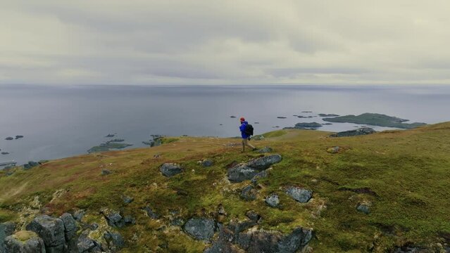 Young male backpacker hikes alone on the top of the fjord and enjoys breathtaking views of Norwegian sea and nordic islands.