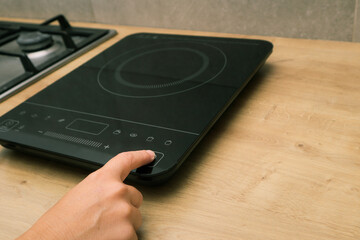 Woman hand turn on induction stove. Finger touching sensor button on induction or electrical hob. Modern kitchen appliance.