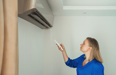 Woman holding remote control aimed at the air conditioner.