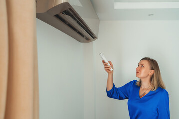 Woman holding remote control aimed at the air conditioner.