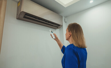 Woman holding remote control aimed at the air conditioner.