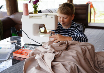 happy smiling handsome boy sewing clothes on a sewing machine at home. Portrait of teenager with sewing machine