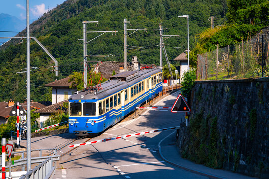 Historic electric train at gated level crossing in Intragna in Centovalli valley. Famous narrow gauge railway line from Locarno to Domodossola in the swiss-italian Alps. Popular tourist train journey