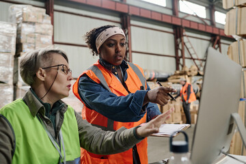 Foreman pointing at monitor and discussing document online with worker during their work in warehouse