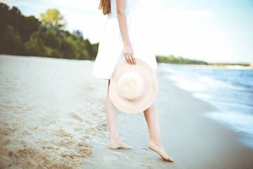 Young woman on a beach holding a white hat. Legs close up - 625998608