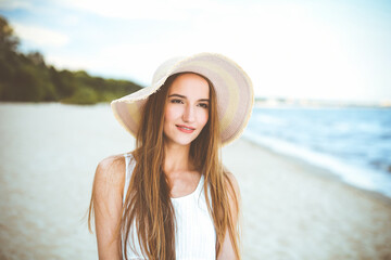 Portrait of a happy smiling woman in free happiness bliss on ocean beach standing with a hat. A female model in a white summer dress enjoying nature during travel holidays vacation outdoors