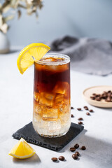 Coffee with tonic in a tall glass with ice and lemon on a light blue background with coffee beans...