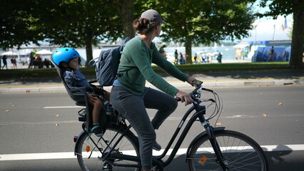Woman riding bicycle in urban street with child in back seat