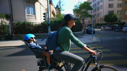 Fototapeta na wymiar Woman riding bicycle in urban street with child in back seat