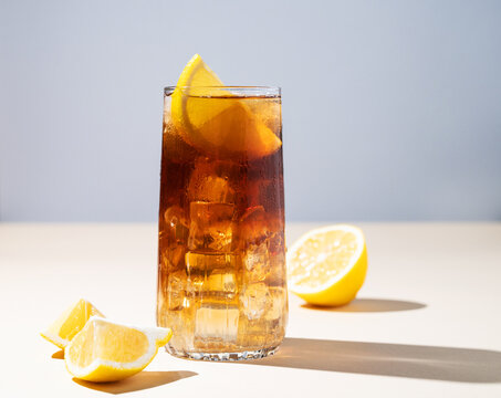 Iced tea with lemon and ice in a tall glass on a yellow background. The concept of a refreshing drink or lemonade on a hot summer day.