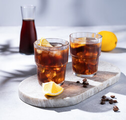 Cold brew coffee in a two glasses with lemon and ice on a marble board on a light background with...