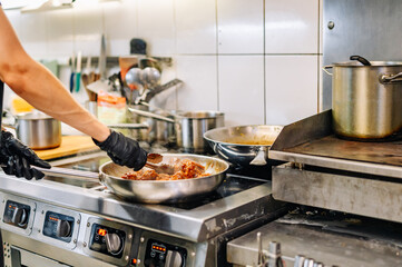 woman chef cooking chicken wings in a sauce in the kitchen
