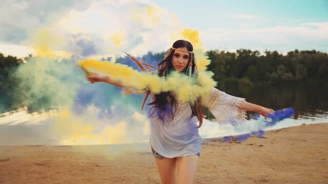 Happy woman dancing waving hands holding smoke bomb colored yellow blue purple color. river bank nature sand beach enjoy life blue sky, long hair headband feather boho style. hippie girl white dress 