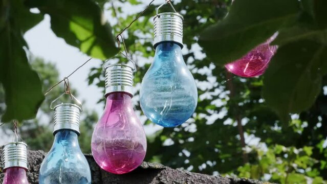 Colorful light bulbs lined up in a row hang on a wire. Light bulbs are red and blue.