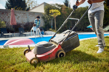 Low section shot of young man mowing grass by the pool, clean cut grass.
