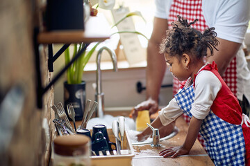 Cute little girl helping her father with the dishes in a domestic kitchen, washing dishes together, working as a team. - 626013887