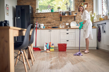 Attractive young housewife wet mopping the floor in the kitchen, cleaning the home.