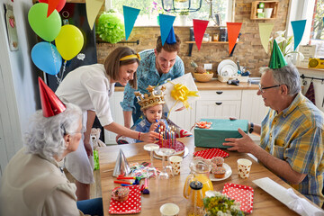 Young princess girl with an inflatable crown on her head, sitting by the table celebrating her birthday with family memebers around. © luckybusiness