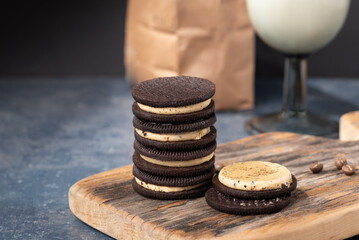 Coffee cream stuffed sandwich cookies stacked on a wooden board with coffee beans and a glass of milk.