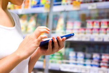 Woman shopping in a supermarket looking at the screen of the phone her shopping list