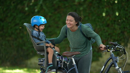 Mother and child loving moment together riding bicycle kid sitting on bike back seat laughing together with mom