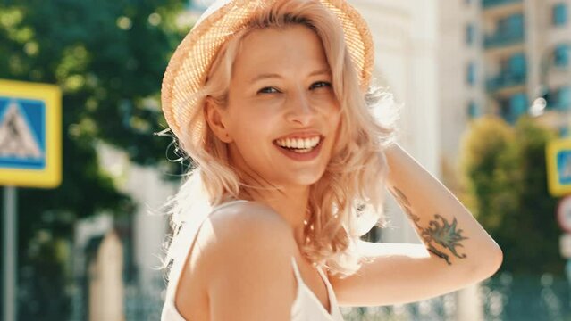 Young beautiful smiling hipster woman in trendy summer white topic clothes. Sexy carefree model posing in the street at sunny day. Positive blond female outdoors. Cheerful and happy. In hat