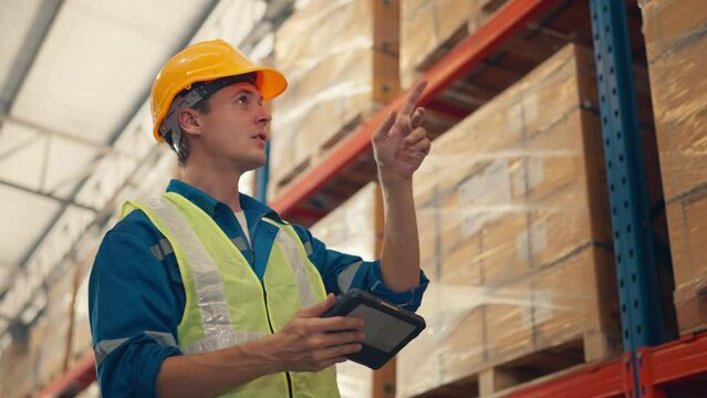 Man worker checks products stock inventory with digital tablet in the retail warehouse full of shelves Male employee wearing hard hat doing work in storehouse.