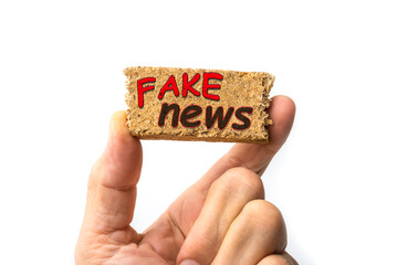 Fake news sign on a piece of wood between fingers