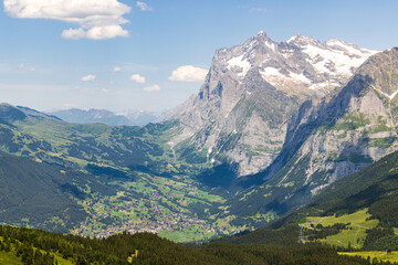 Naklejka premium The small village of Grindewald as seen from a hiking trail in Switzerland with blue skies and a mountain in the background