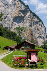 A small stall selling goods and a chalet with a mountain and waterfall in the background