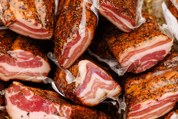 Cured meat wrapped in plastic sits in a pile on a farmer's market table