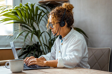 One woman at home in office workplace table using laptop and headset for voice and video call with clients for small business concept lifestyle. Modern female people entrepreneur working alone online