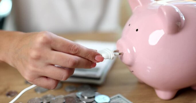 Hand with an electric fork and pink piggy bank, close-up, slowmotion. Saving energy, alternative electricity