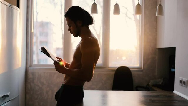 sexy man with naked torso reading a book at home, self education and personal development concept.