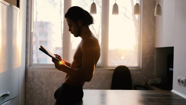 sexy man with naked torso reading a book at home, self education and personal development concept.