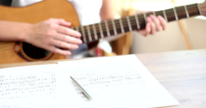 Notes and a pen are on the table, close-up, slowmotion. Man plays the guitar and composes music, shallow focus