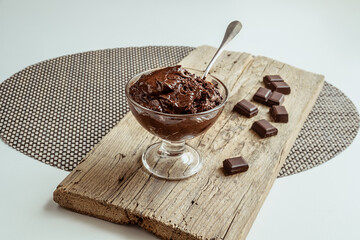 A transparent bowl with chocolate mousse, traditional French dessert and pieces of dark chocolate on a wooden board
