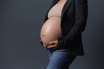 Close-up of beautiful pregnant belly in pregnancy 36 week, isolated gray studio background. Copy ad...