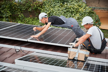 Men technicians mounting photovoltaic solar moduls on roof of house. Electricians in helmets installing solar panel system, tightening with hex key. Concept of alternative and renewable energy.