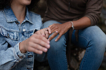 A woman rests her hand on her partner's knee, holding each other's hands. They are a queer,...